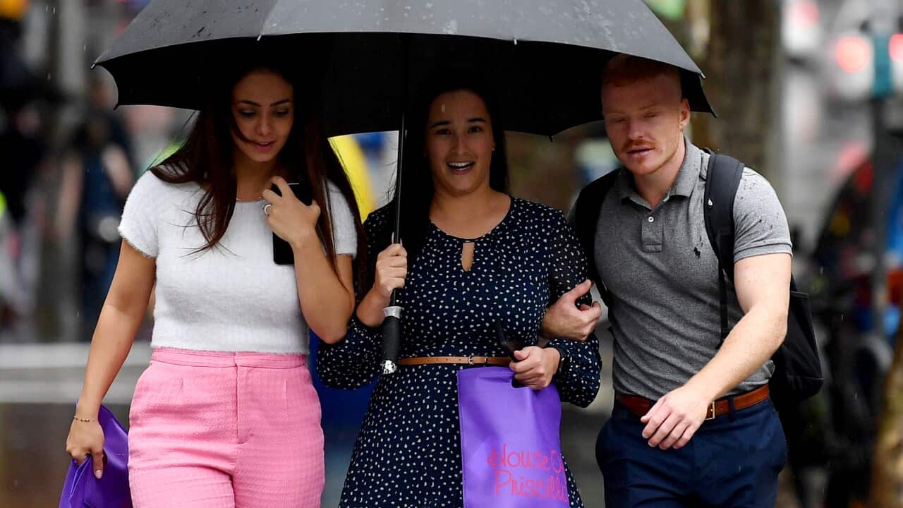Three people walking along a footpath. One is holding an umbrella.
