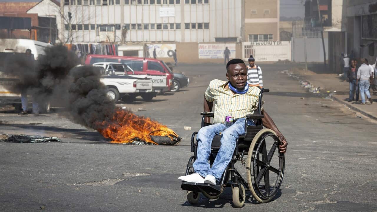 A protester in a wheelchair passes a burning tyre in Johannesburg