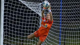 A woman in an orange football uniform catches a ball mid-air