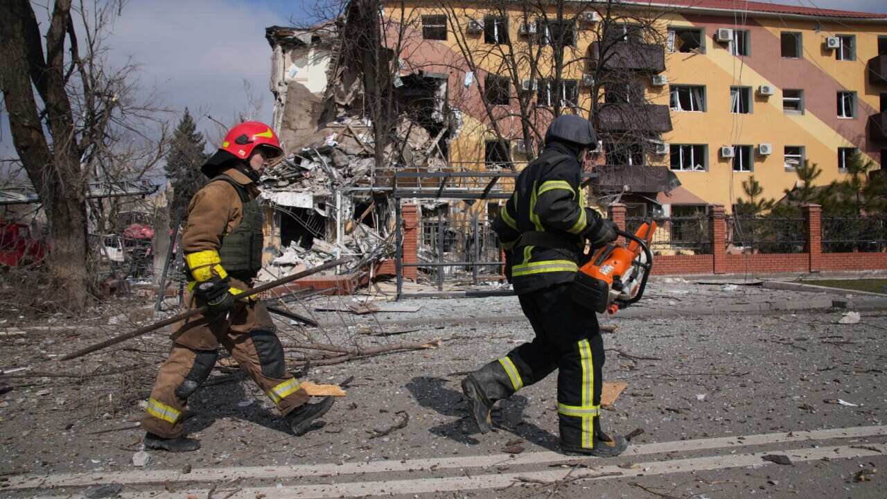 Firefighters walk past a damaged by shelling building in Mariupol, Ukraine, Thursday, March 10, 2022.