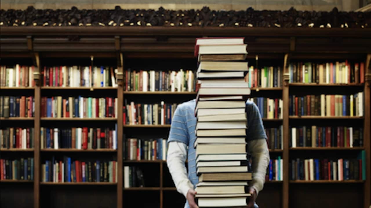 Young man carrying stack of books in university library