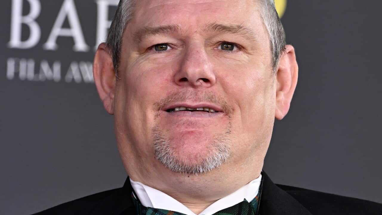 A head-and-shoulders shot of a man in a suit looking at the cameras with a slight smile on his face.