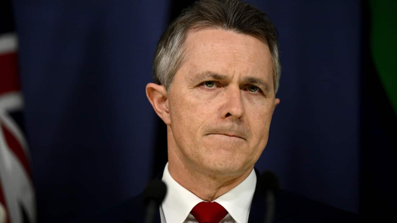 A man, wearing a suit and tie, is standing in front of a microphone attached to a lectern.