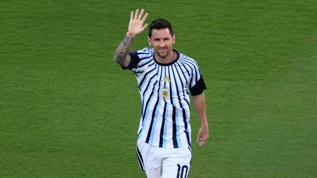 Footballer Lionel Messi, dressed in a blue and white striped training uniform, waves before a match at the 2026 World Cup.