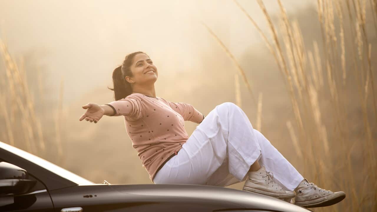 Smiling woman sitting on car hood during weekend at sunset