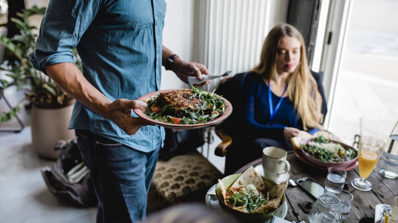 Waiter Serving Food To Customers Sitting Down