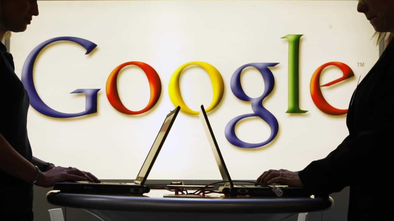 People working on laptops in front of the Google logo