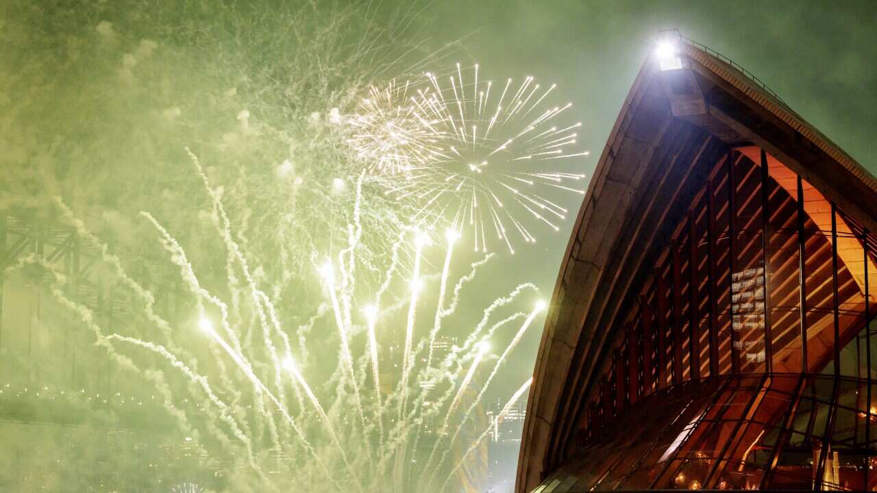 People standing outside the Sydney Opera House as fireworks go off