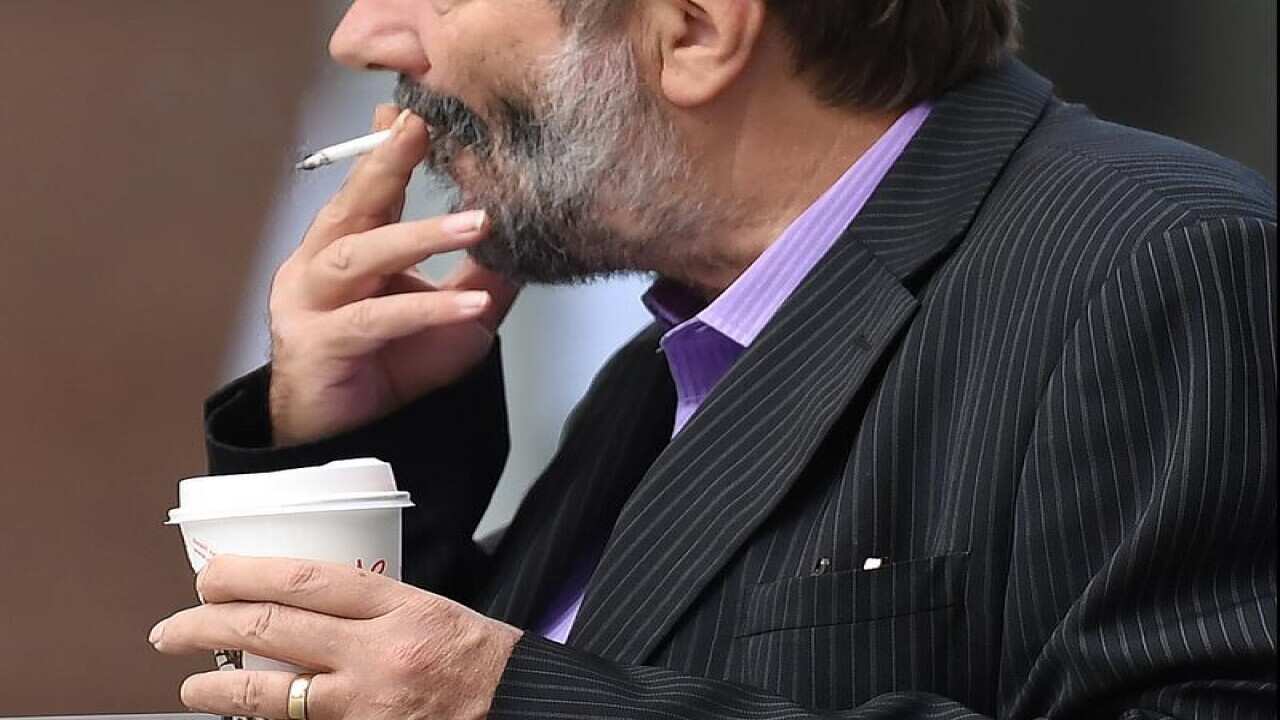 A man smoking and holding a cup of coffee