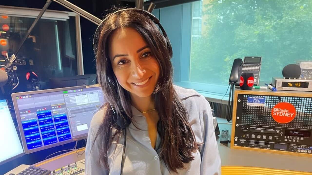 A woman wearing headphones and a blue shirt smiling for the camera in a radio studio.