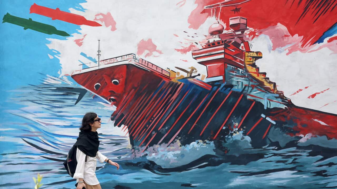 A woman in sunglasses walks past a mural of a warship