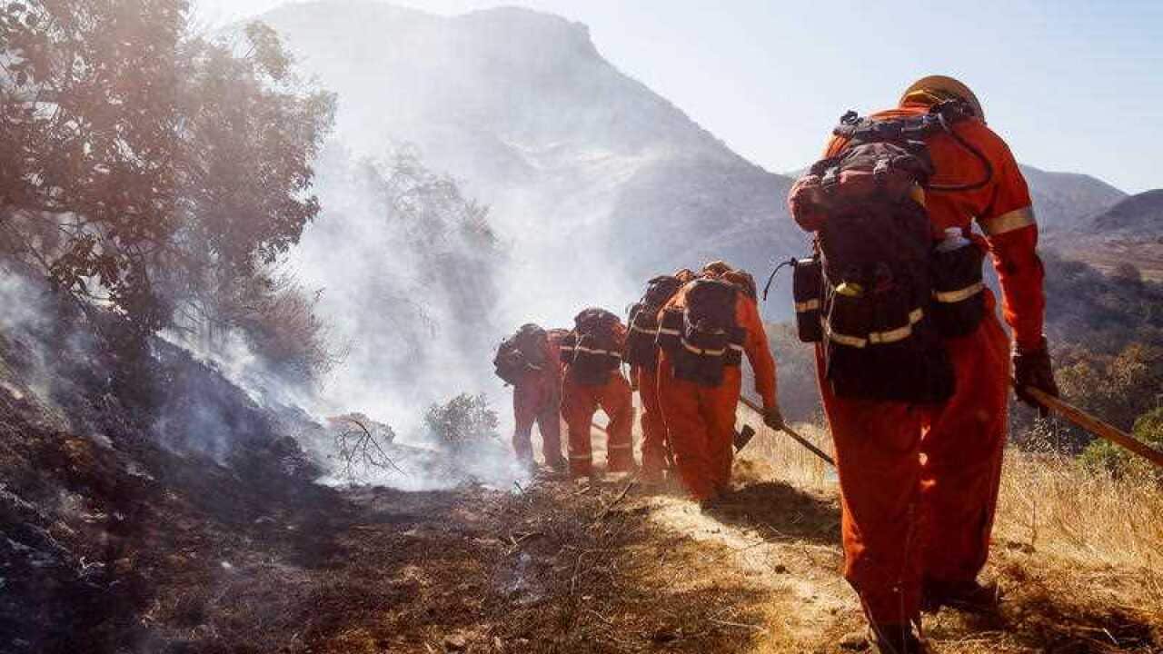 Firefighters work to extinguish a flare-up of the Woolsey Fire on a hillside in West Hills, California,