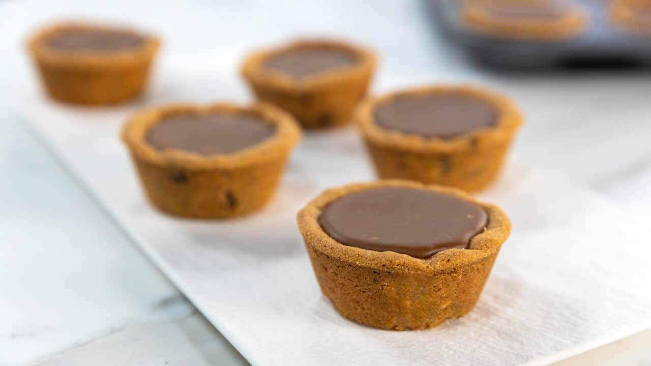 Two rows of tartlet-shaped cups sit on a platter, with a biscuit-like shell and a dark caramel filling.