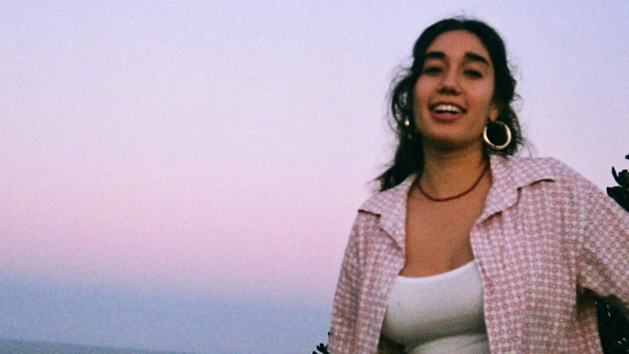 Maya Skidmore wearing a white fitted top and a baggy pink and white checkered oversized shorts at sunset. 