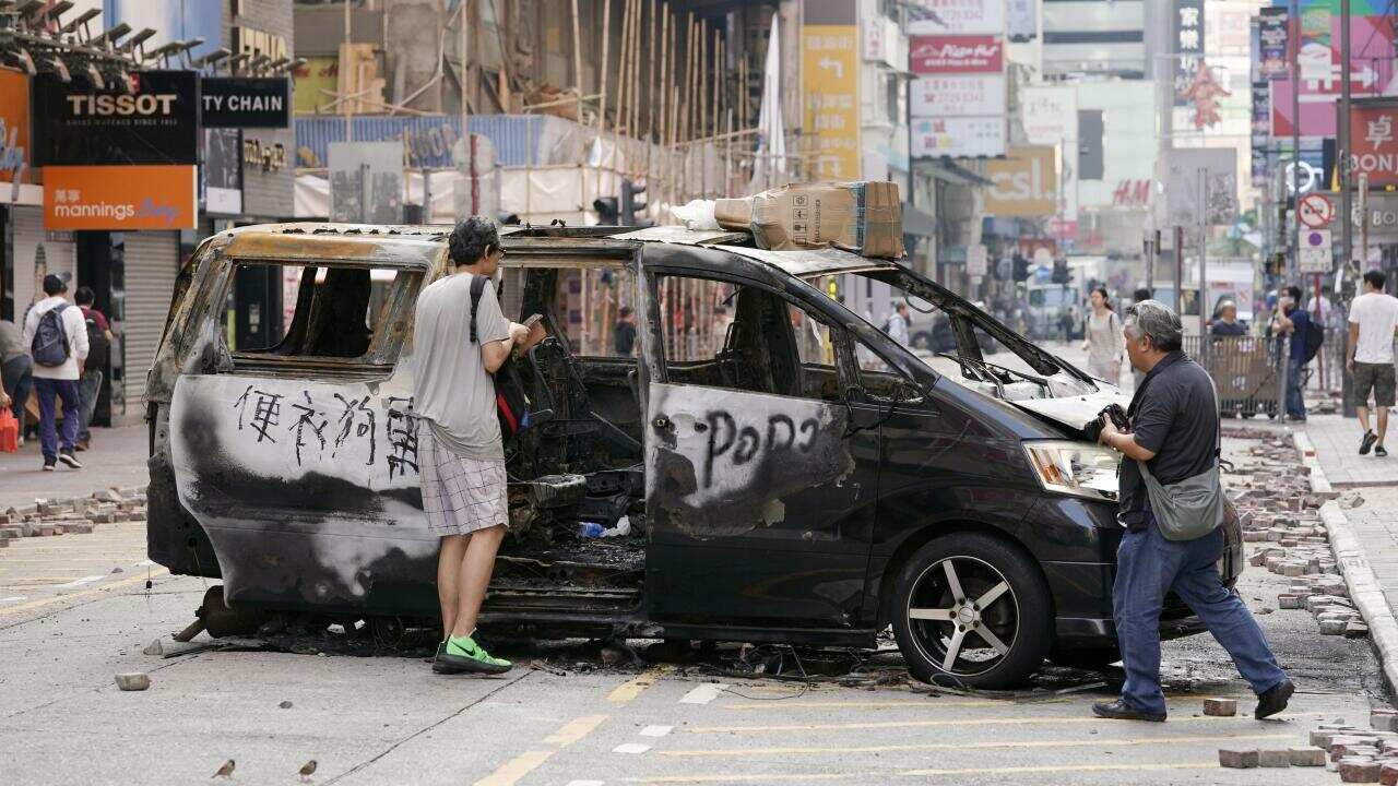 Passersby look at a burned-out car on a street in Hong Kong.