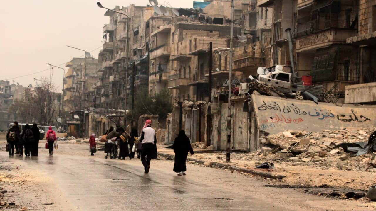 Syrian people walk a street in Aleppo near Arabic inscription written on a damaged building reading 'Aleppo is bleeding, I will not give up your soil'