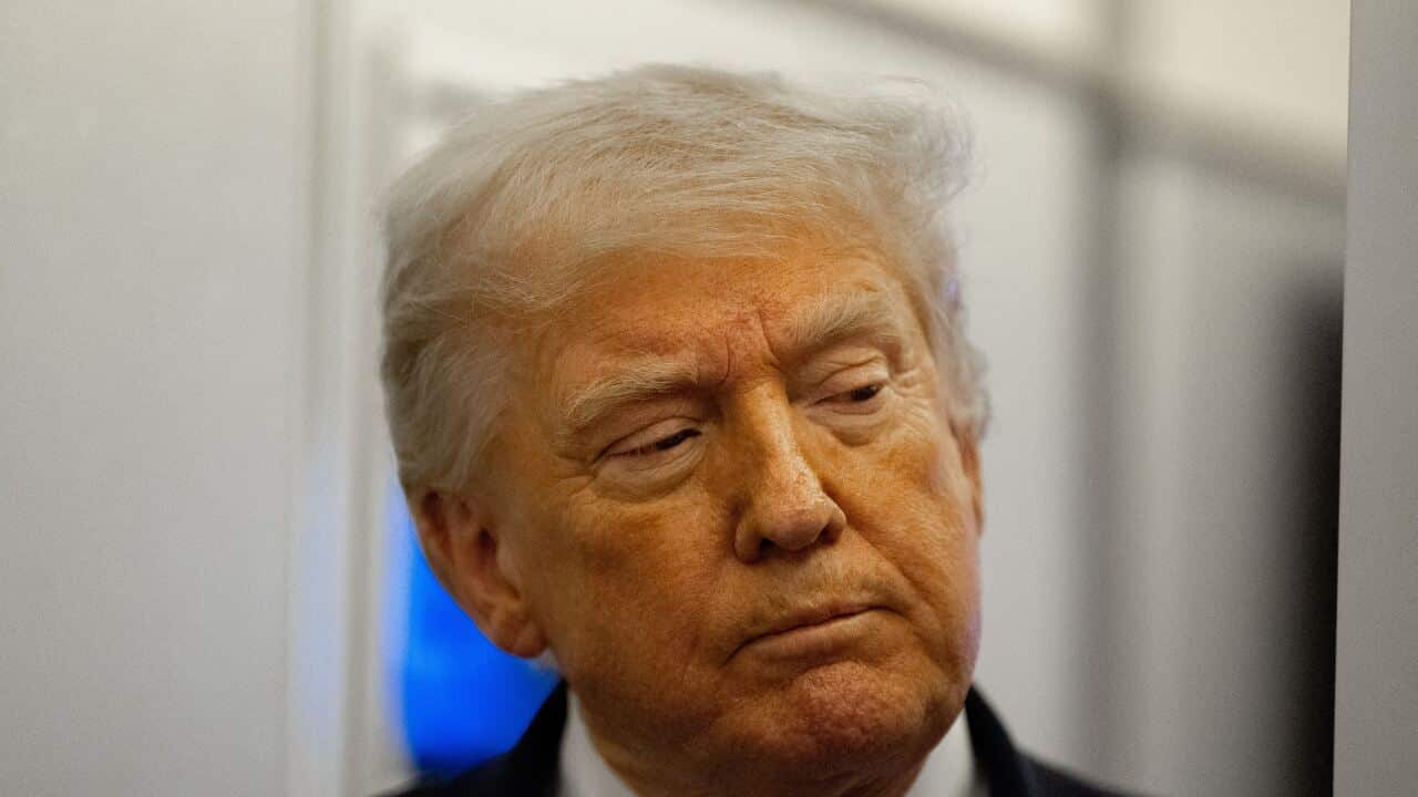 A close-up, slightly high-angle shot of Donald Trump looking downward with a sombre expression against a blurred indoor background.