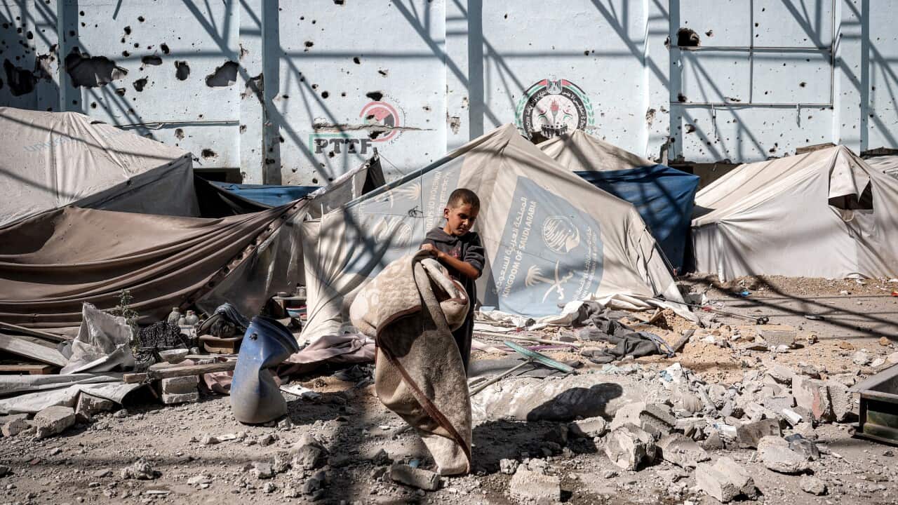 A boy carries away a blanket as he walks past shelter tents in Gaza.