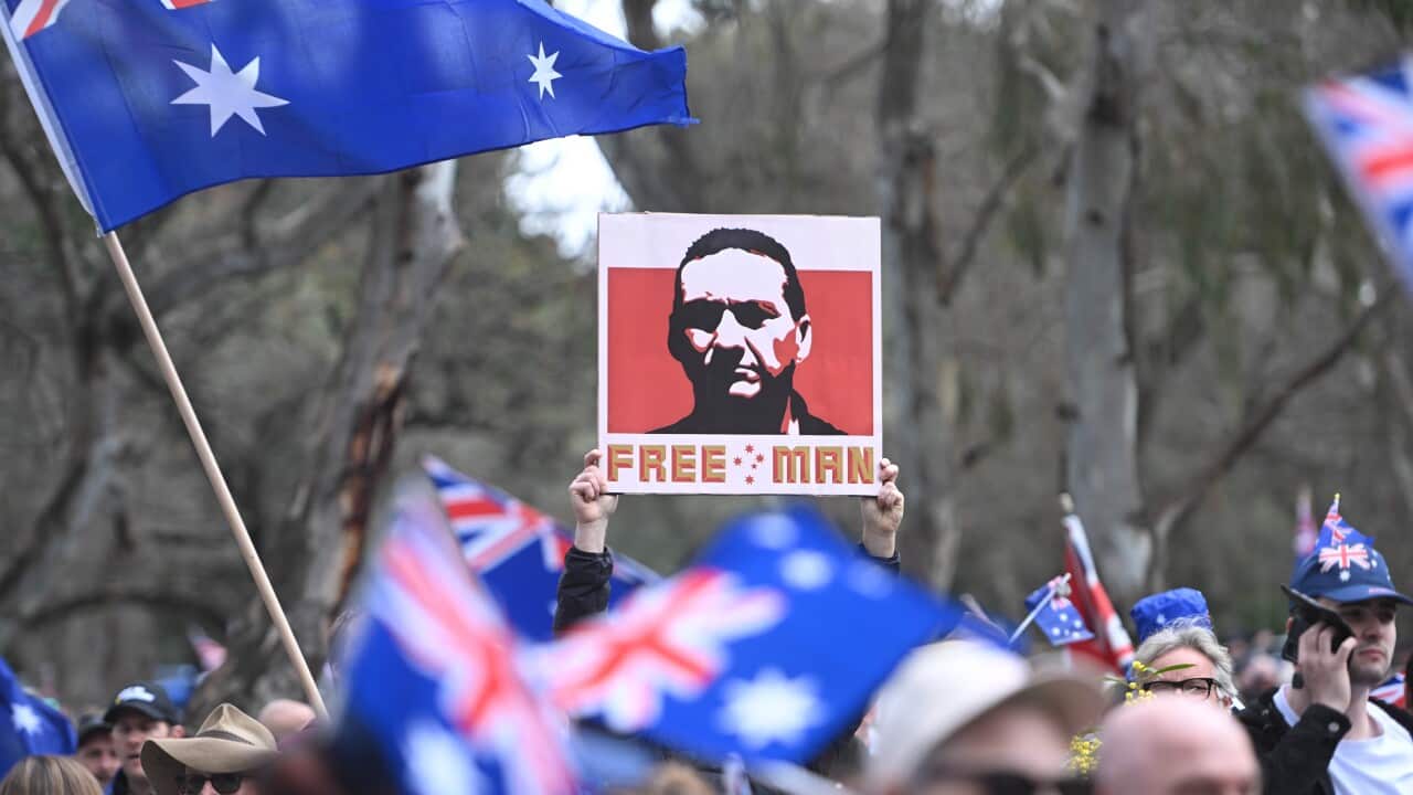 A protestor holds up a sign featuring a stylised portrait of Dezi Freeman and the words "FREE MAN" amid a crowd waving Australian flags.