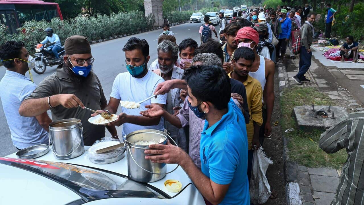 Daily wage labourers who are out of work during COVID-19 lockdowns, queue up as volunteers distribute food along a New Delhi roadside on 20 May.