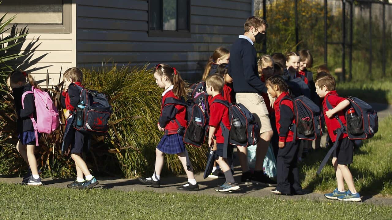 Primary school students wearing uniforms and backpacks enter a school.