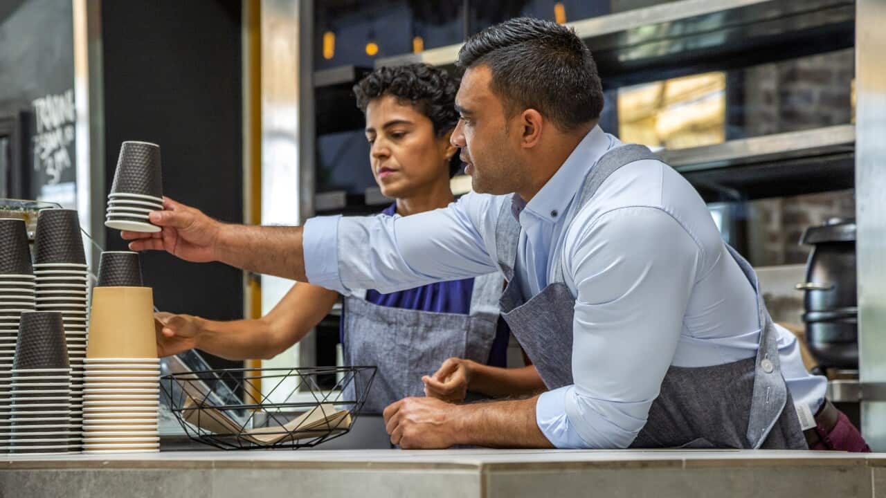 Two cafe owners/workers (small business), working behind counter preparing food & drinks