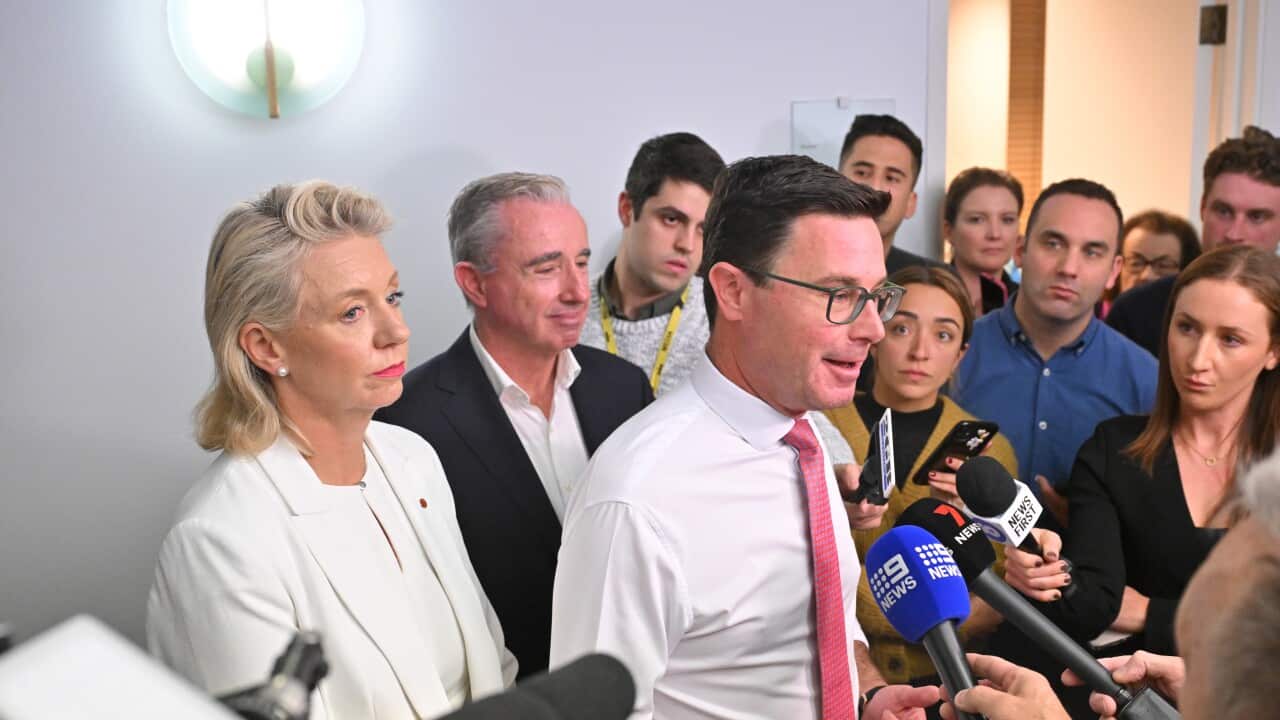 A group of people is next to a man in a white shirt, speaking into microphones.