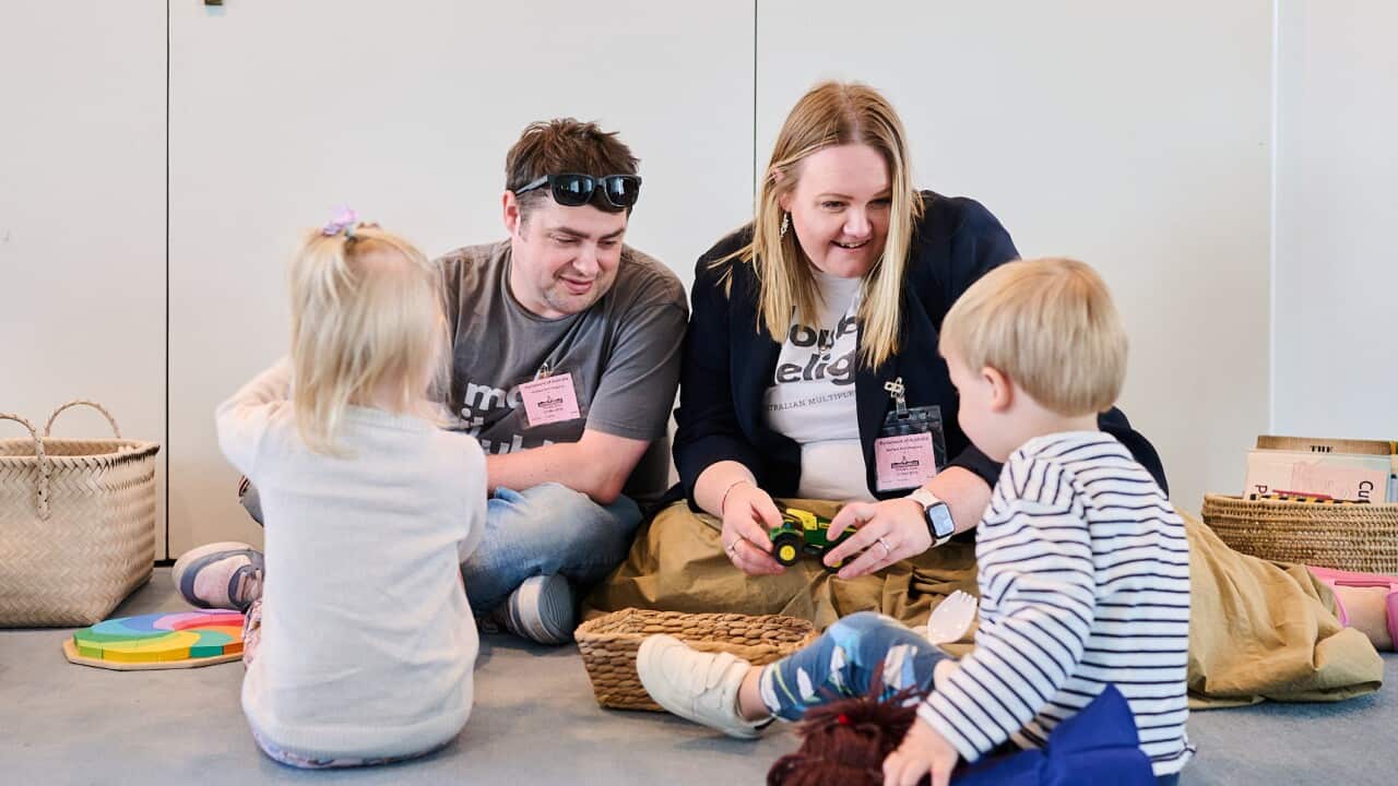 A man, woman and two toddlers sit on the floor and play happily together with toys.