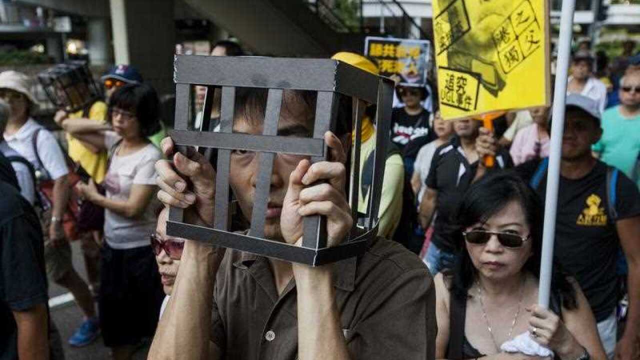 Hong Kong people and lawmakers march through the streets wearing prison uniforms and 'cages' on their heads
