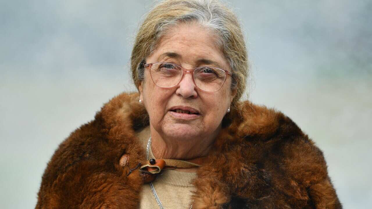 A woman in a fur coat addresses the media with a serious expression.