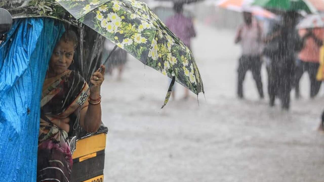 Indian people cover themselves under umbrellas in a flooded street.