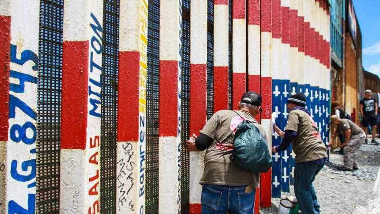 People help repaint a mural on the border fence between Mexico and the United States in Tijuana, Meixco.