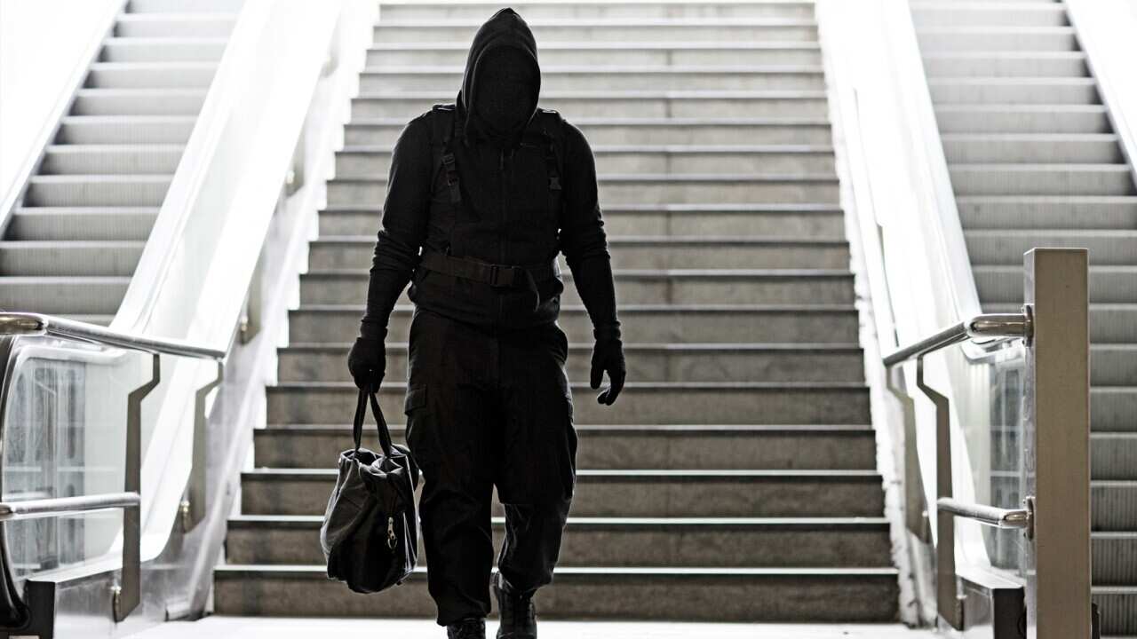 Hooded Lone wolf Man wearing black carrying bag in urban underground public transport setting