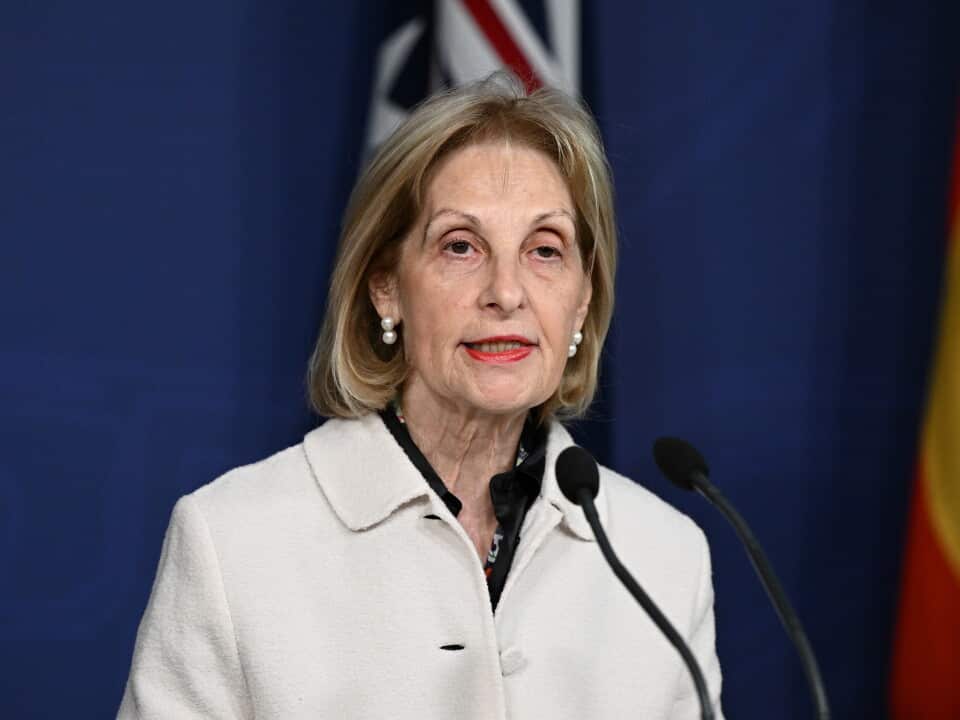 A woman with short blonde hair speaking into a microphone at a podium.