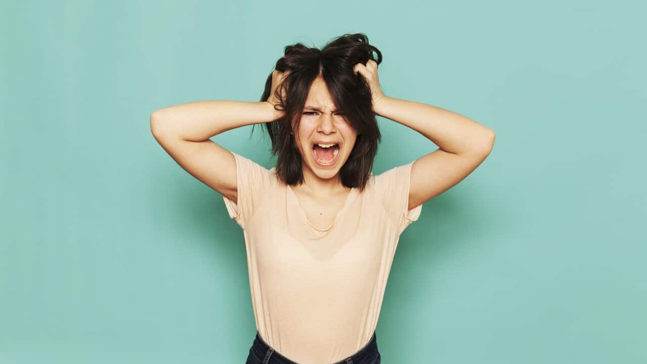 Portrait of frustrated girl shouting with hands in hair against turquoise background