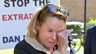 A woman in a black coat with white trim wipes her eyes, crying outside a court building