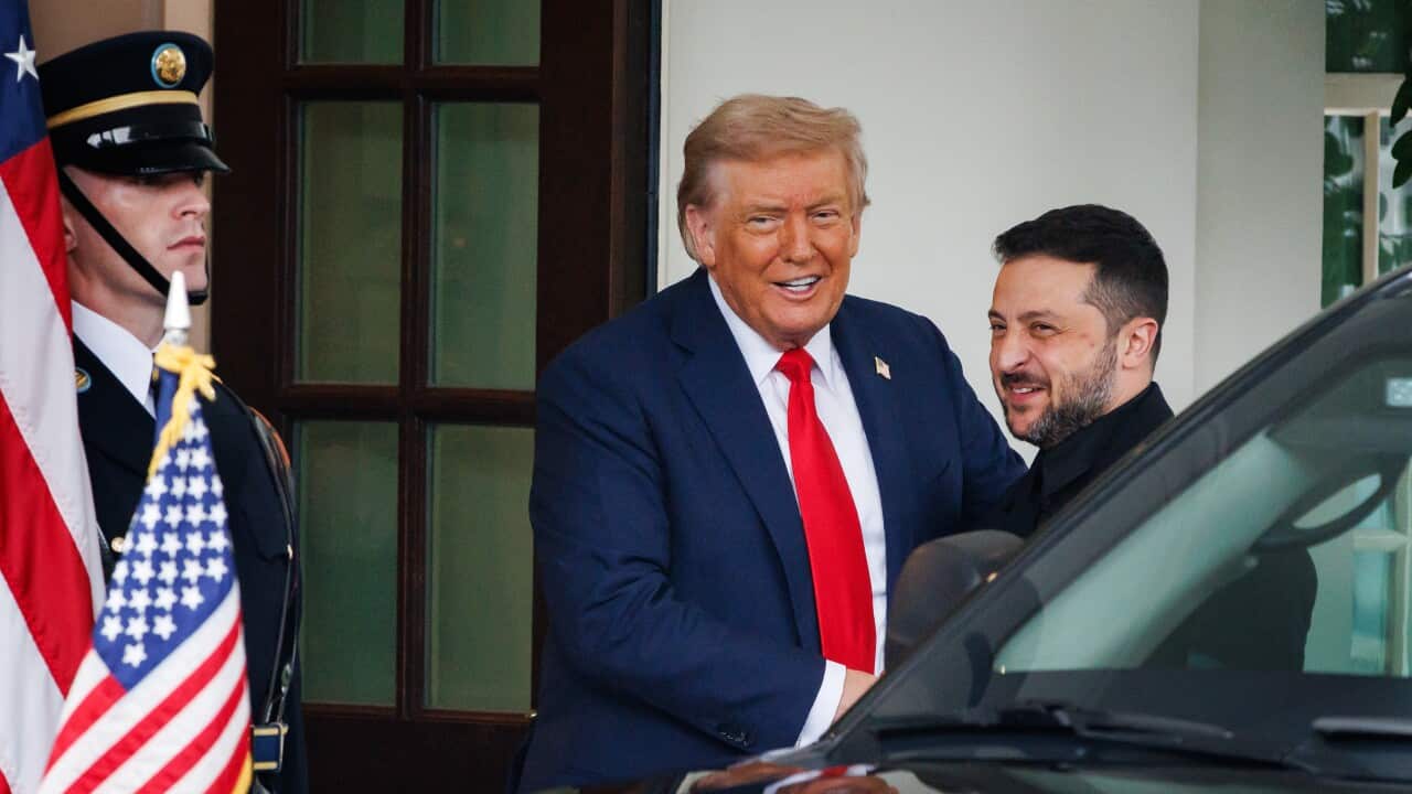 Donald Trump and Volodymyr Zelenskyy smiling as they stand next to a black vehicle and a security guard.