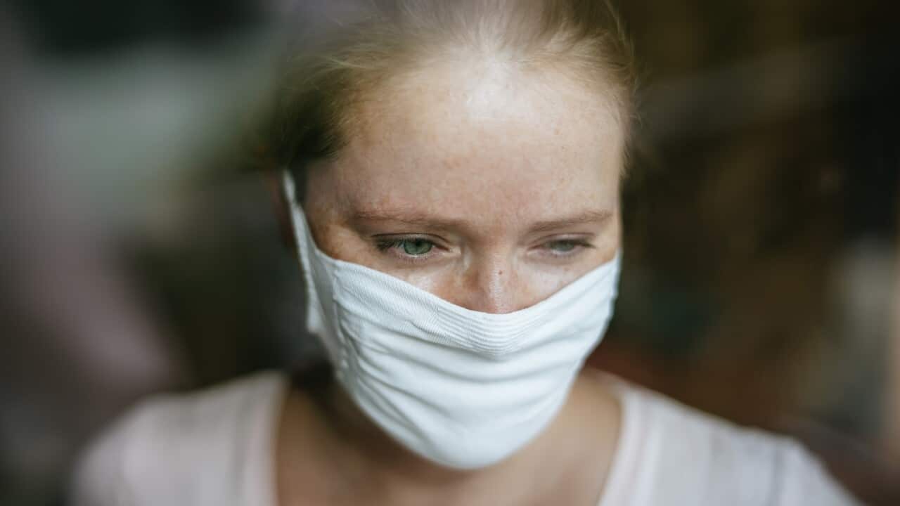 Woman with mask behind window.