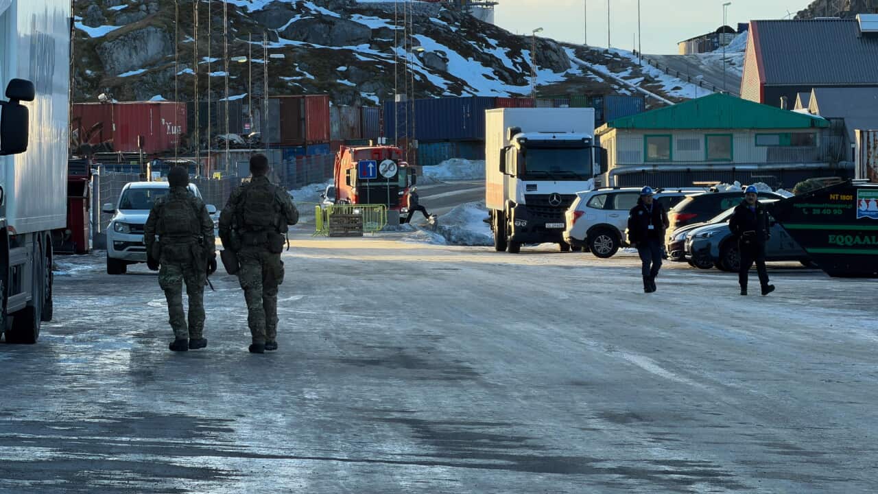 Soldiers walking on a road covered in ice. In the background, there trucks, cars and small buildings,