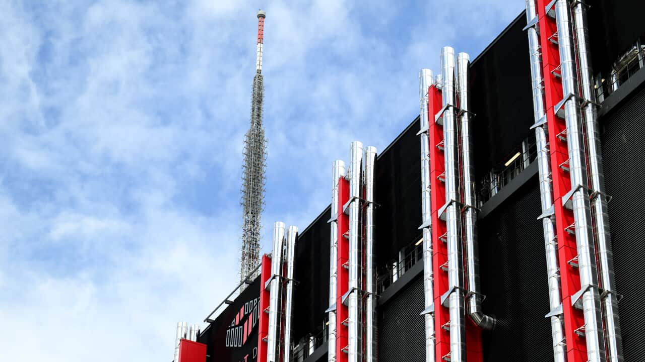 A black and red building covered in pipes with a large metal spire on its roof.