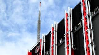 A black and red building covered in pipes with a large metal spire on its roof.