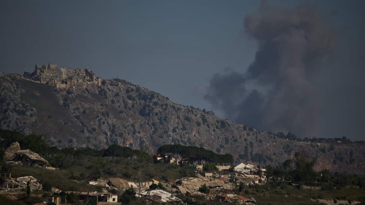 A rocky, hilled countryside with a large cloud of grey smoke rising behind it.