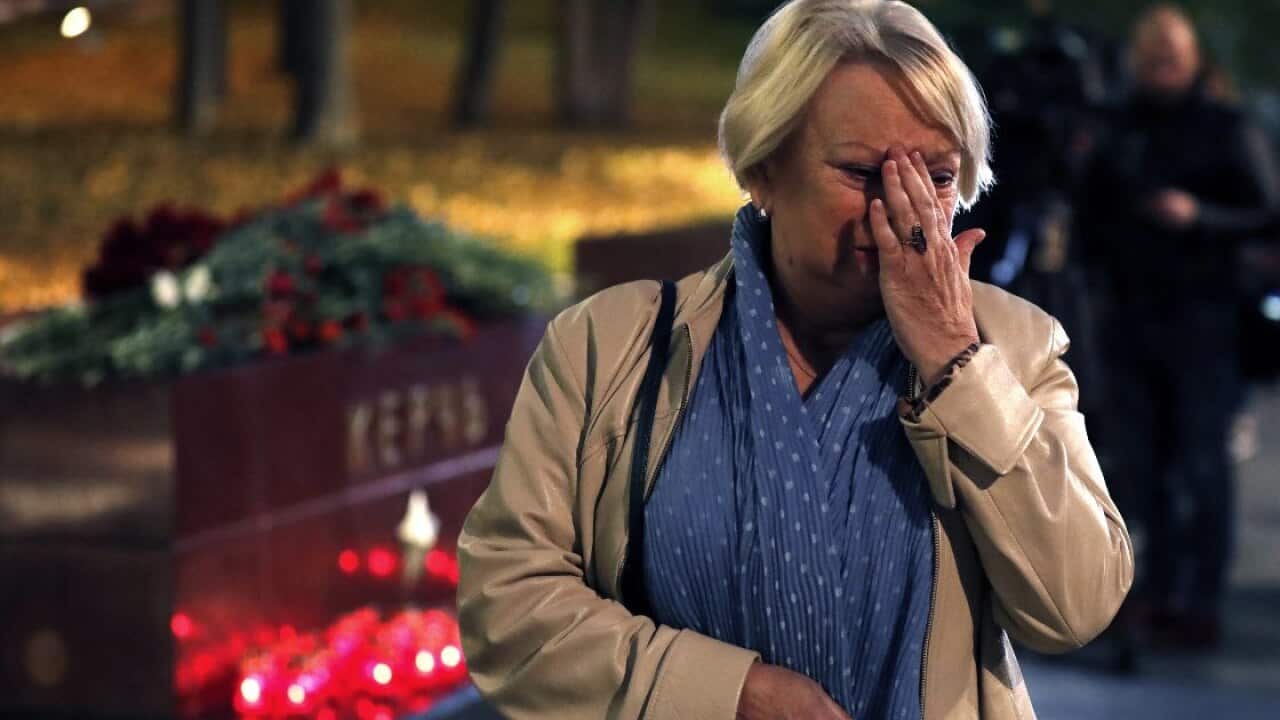 A Russian woman reacts as flowers and candles lay as a sign of mourning for the dead children at a vocational school in Kerch in Crimea