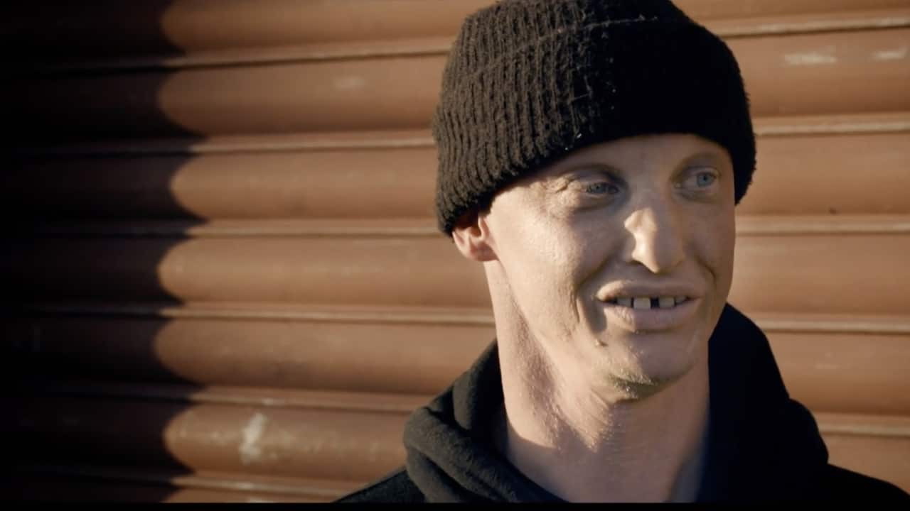 The 'Nek Minnit' guy in a black beanie against a brown roller door