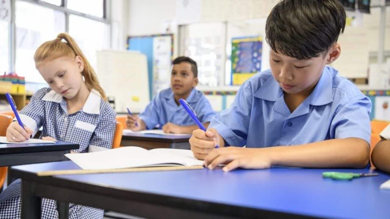 Multi racial school children sitting at their desks and writing in books