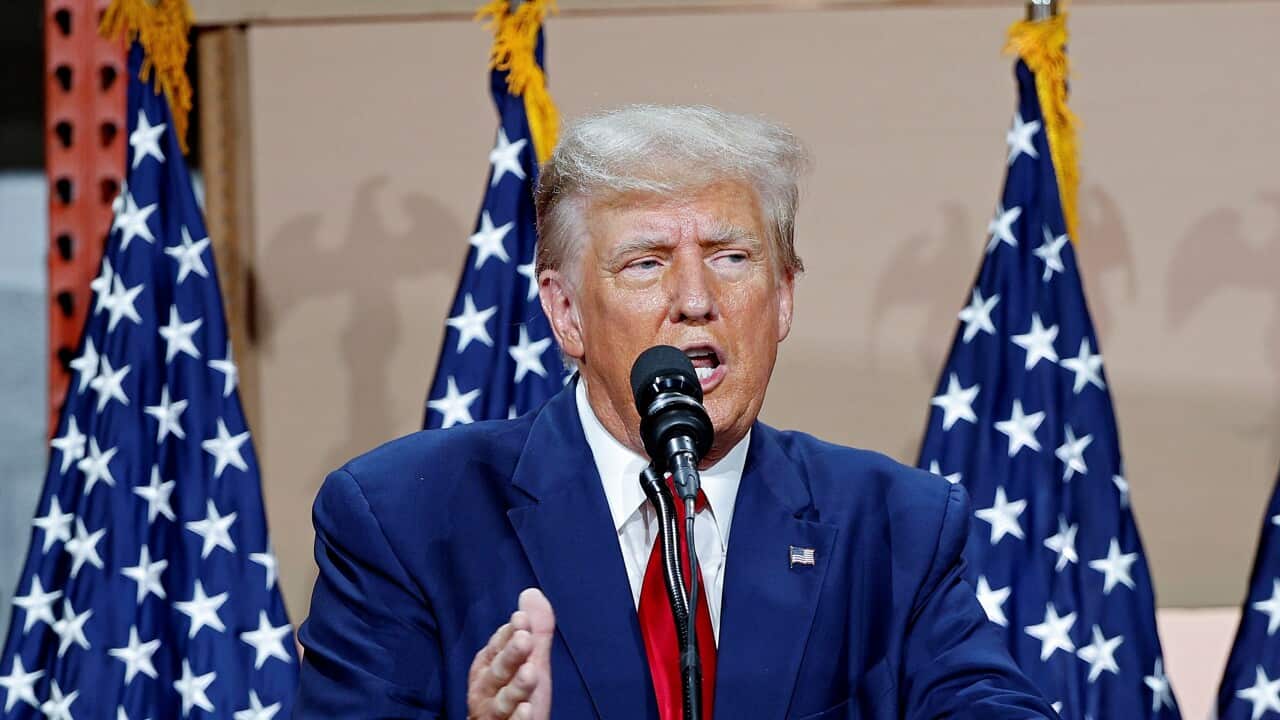 Donald Trump standing in front of American flags and speaking into a microphone.