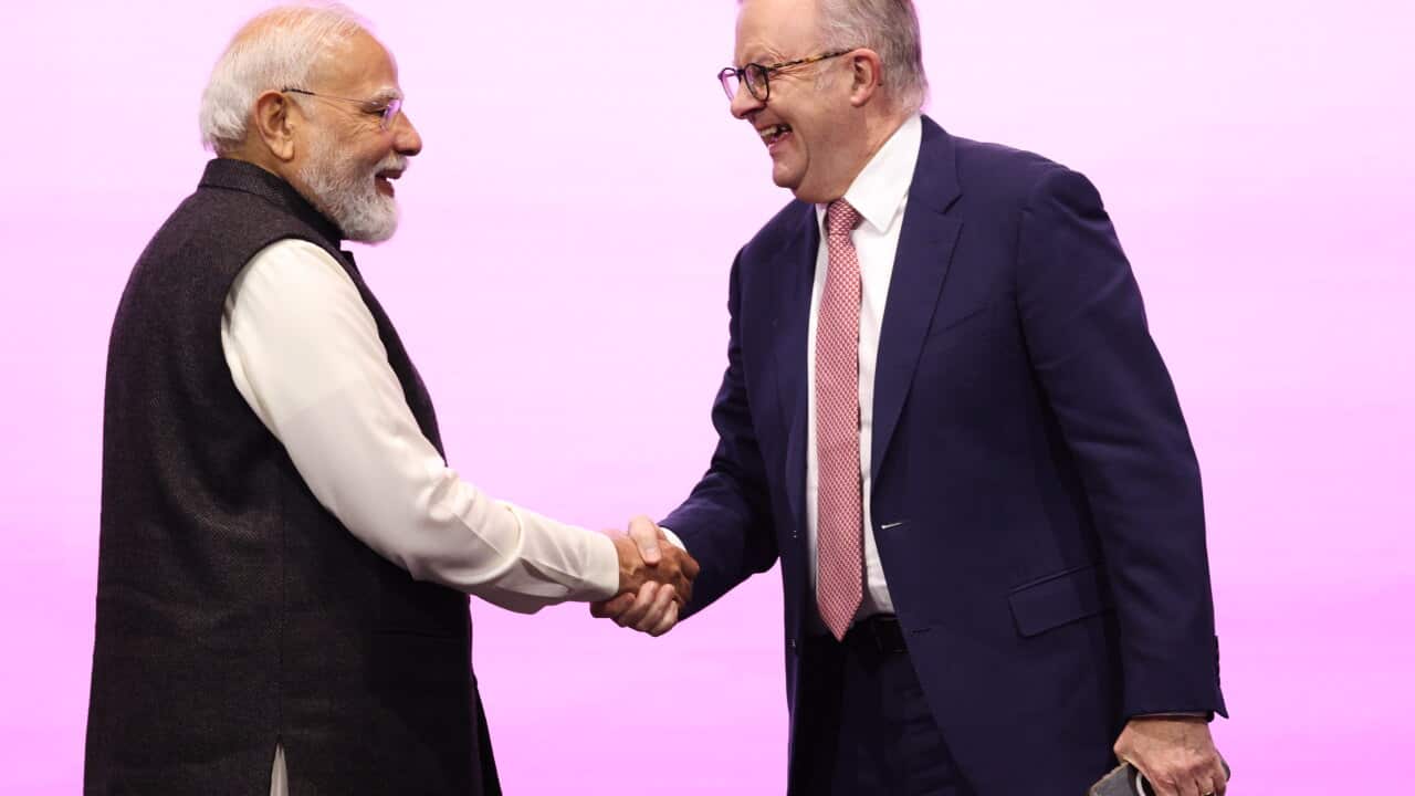 Narendra Modi on the left and Anthony Albanese on the right, they're shaking hands in front of a bright pinkish background