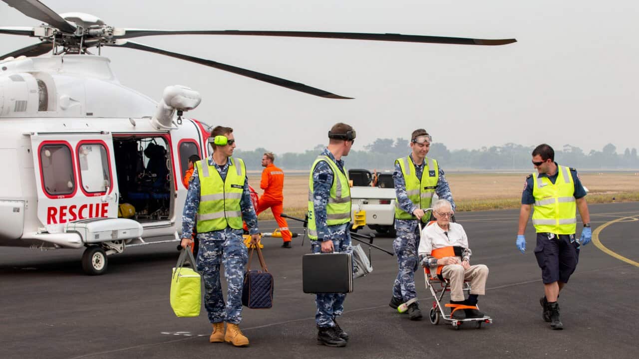 RAAF airmen and a paramedic help an elderly evacuee