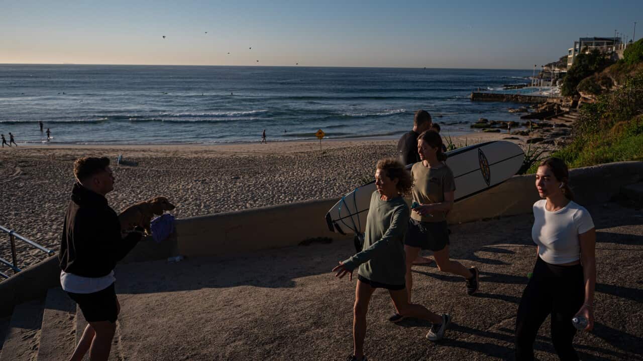 A group of people walking alongside the pavement at a beach.