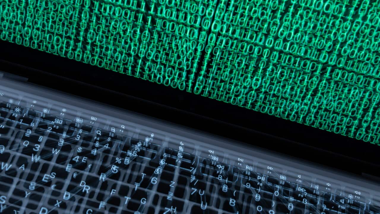 A motion-blurred close-up of a laptop keyboard beneath a screen filled with rows of green binary code.